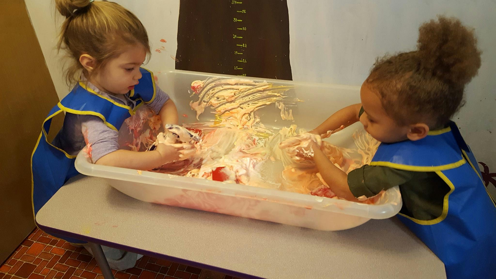 Two children playing with a sensory bin filled with foam