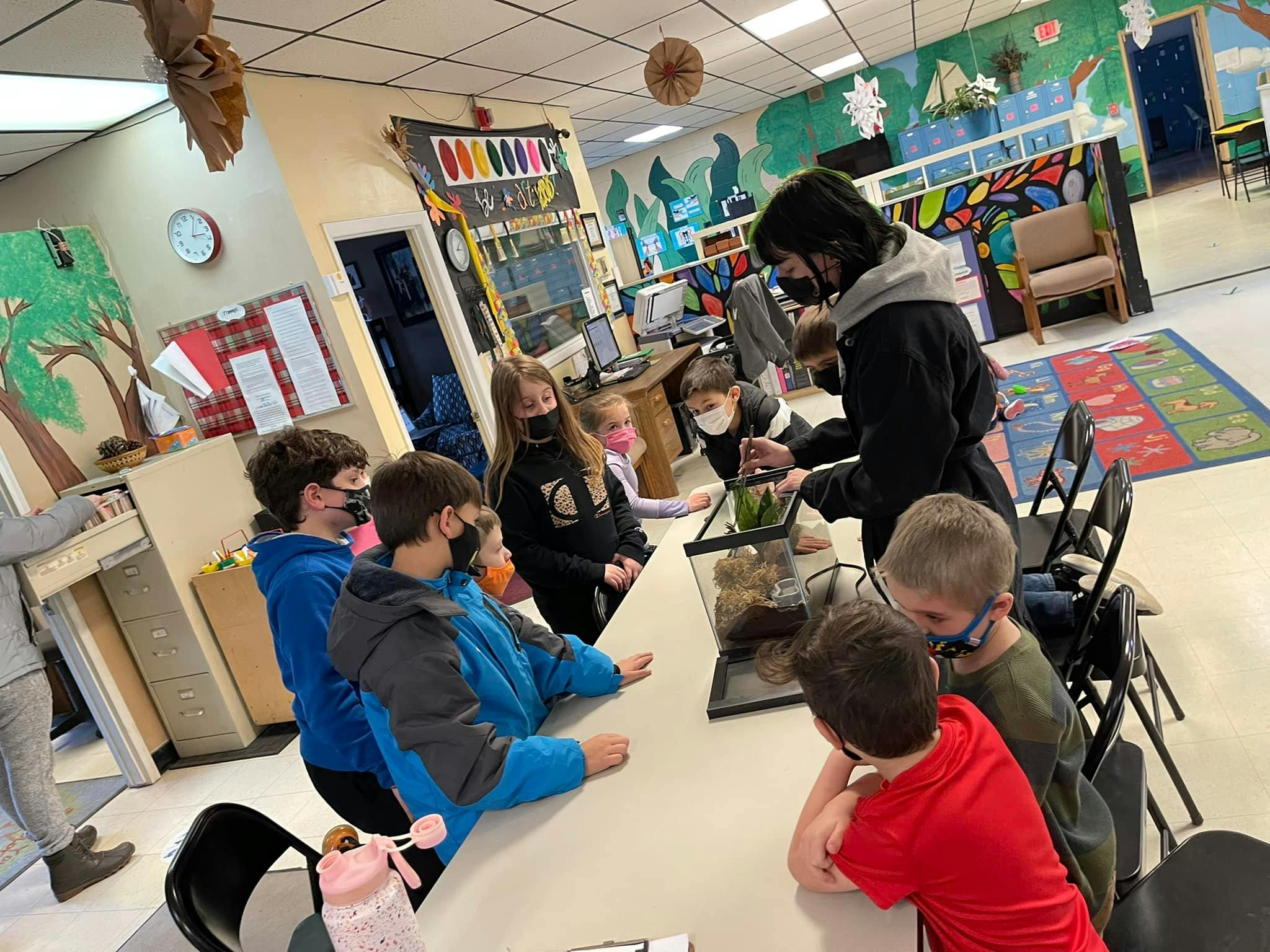 Adult and children gathered around a terrarium in a classroom