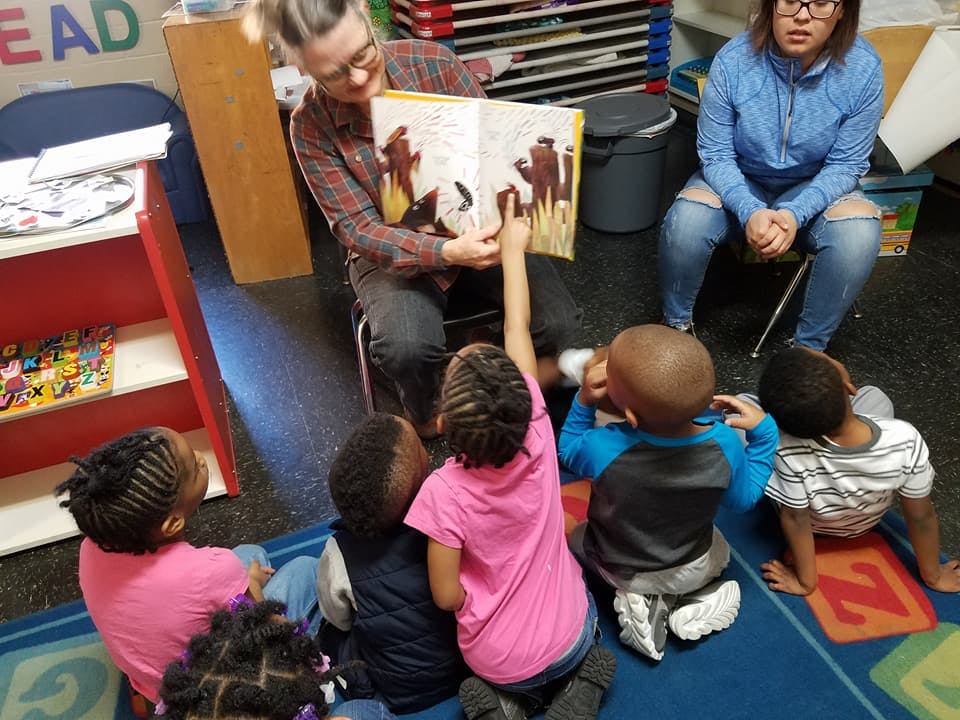 Person reading a book to children in a classroom