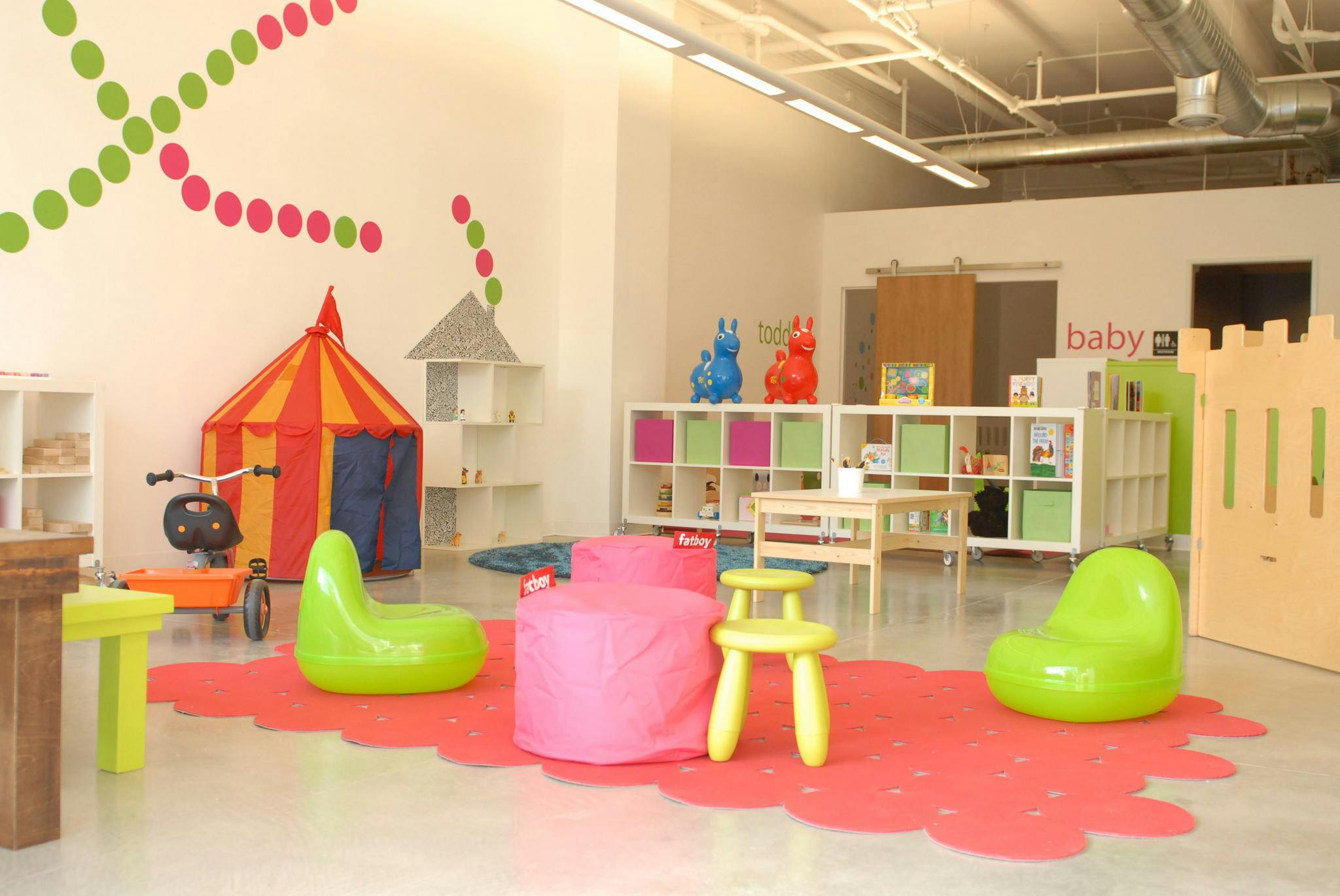 Playroom with colorful furniture, a play tent, and shelves with "baby" on the wall
