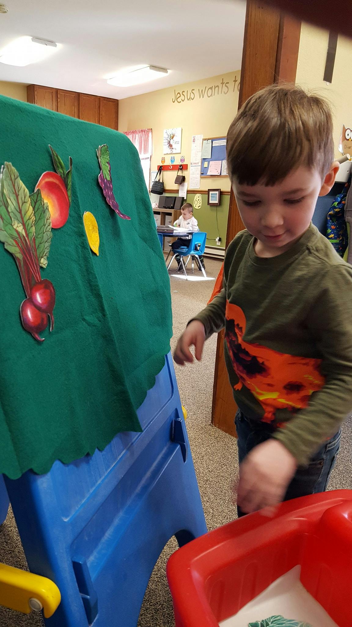 Child standing next to a green fabric board with vegetable cutouts