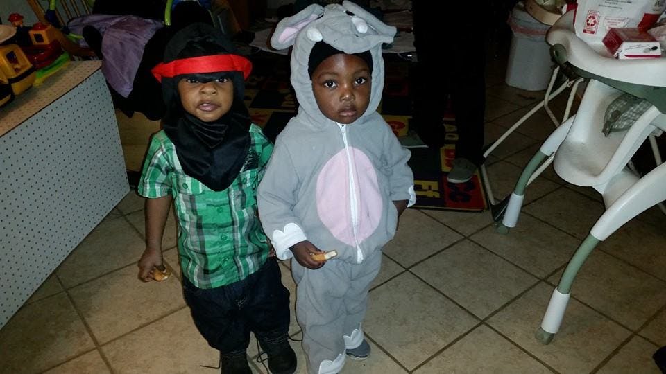 Two children in costumes, one in a green plaid shirt and black hat, one in an elephant costume
