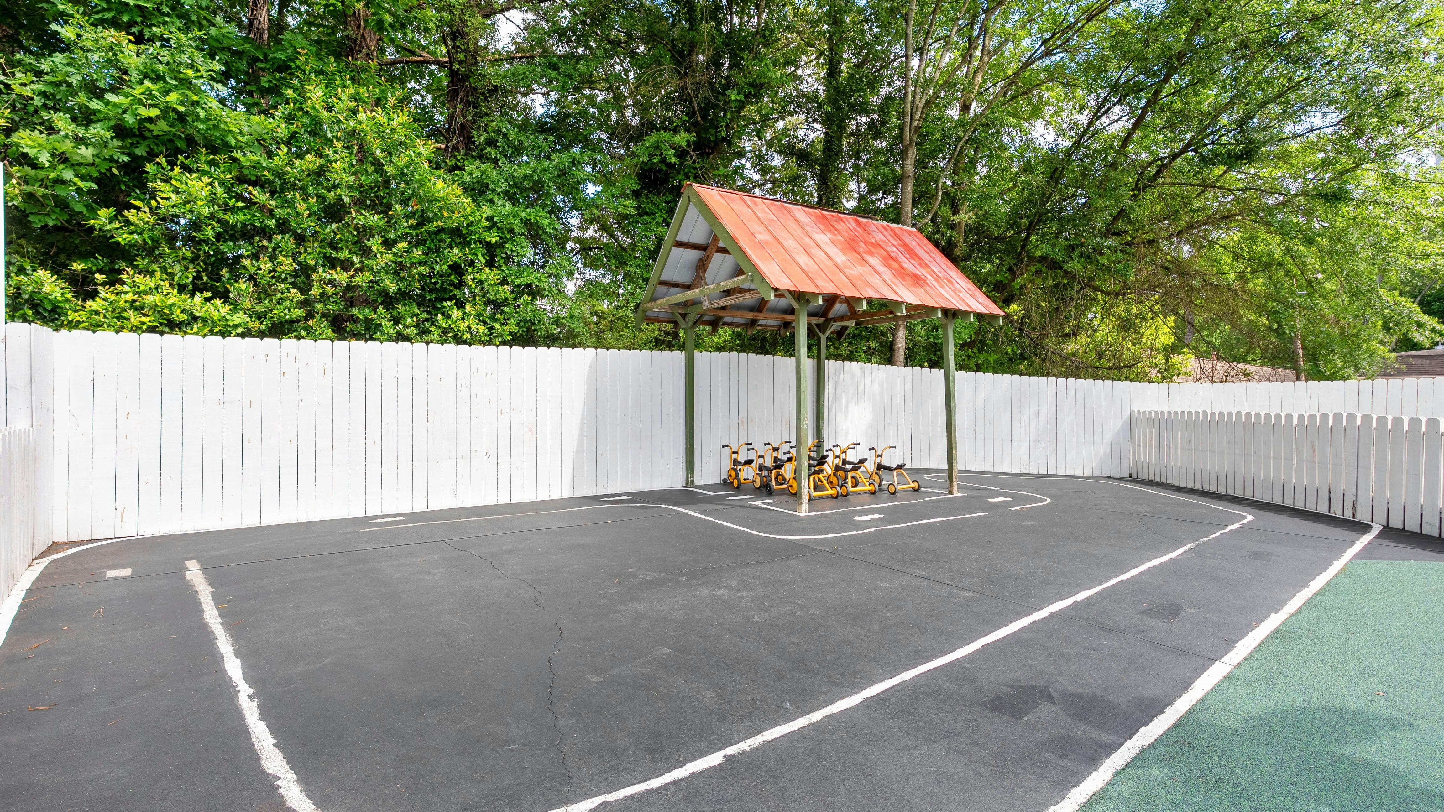Empty children's playground with tricycle track, covered bike parking, and white fence
