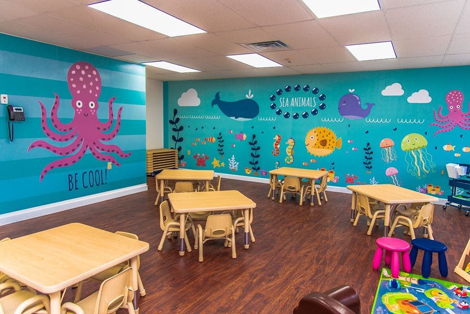 Classroom with small tables and chairs, ocean-themed wall murals