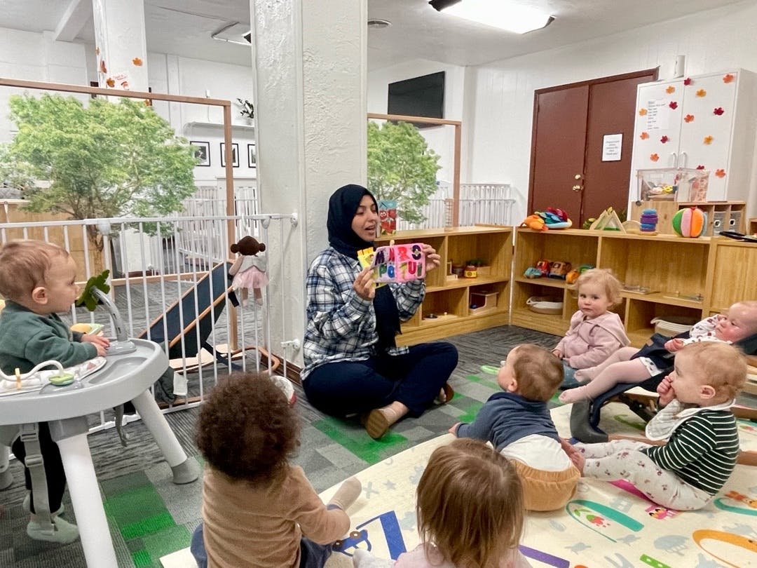 Person holding up a colorful alphabet block to a group of infants in a classroom