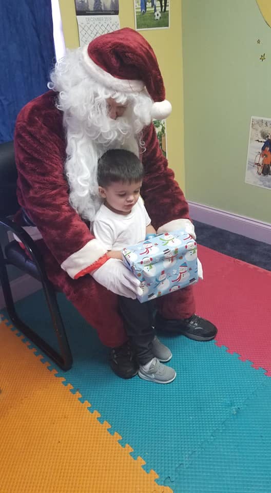 Person in Santa costume holding a child with a wrapped gift