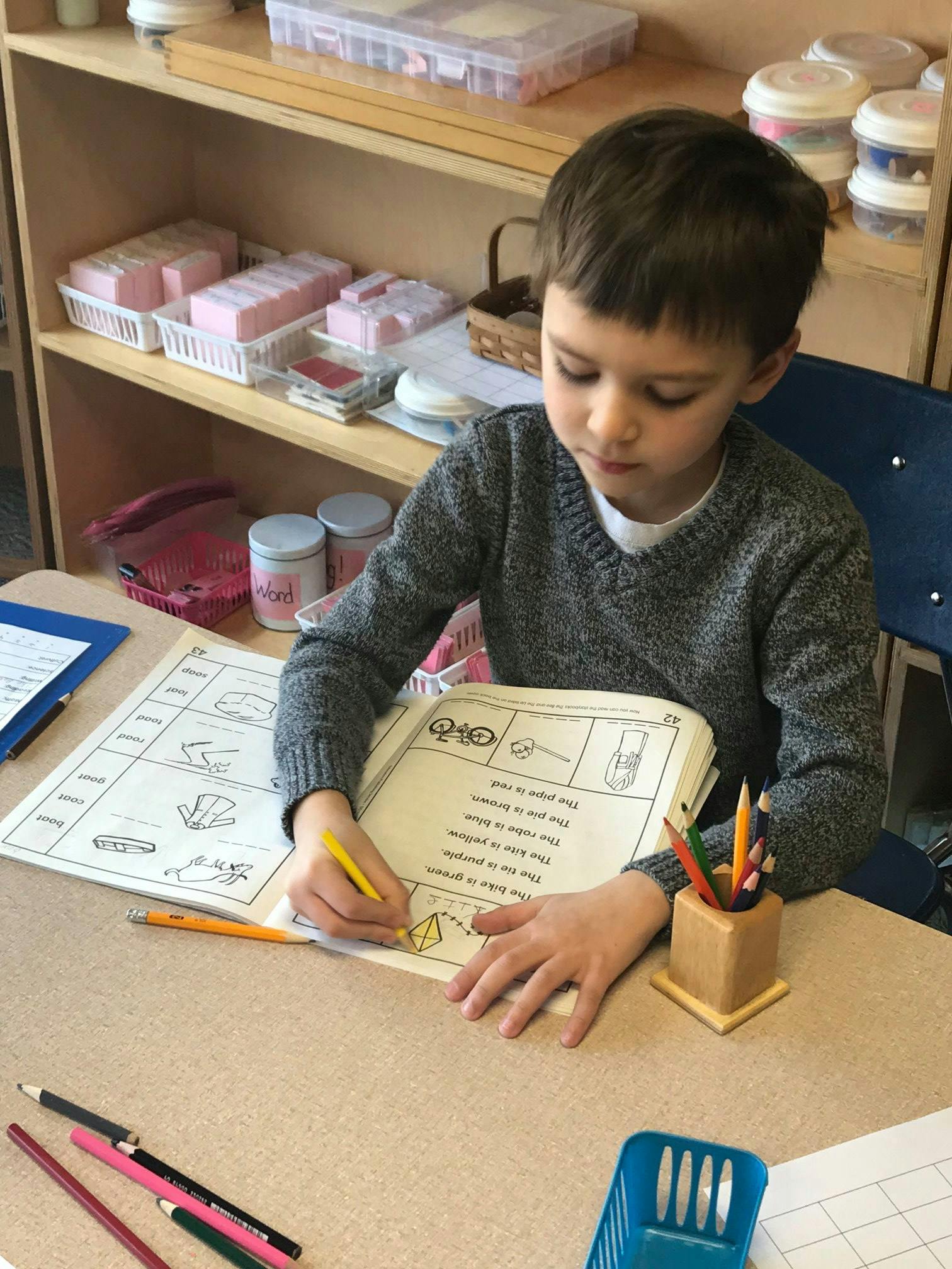 Child coloring a worksheet at a desk in a classroom