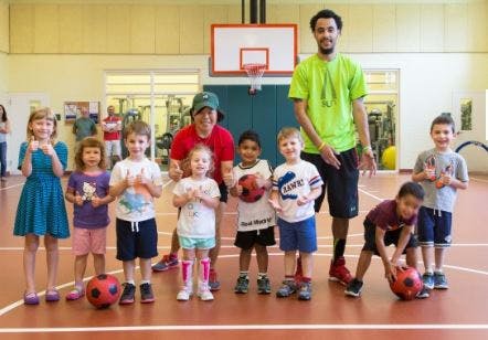 Adults and children posing with soccer balls in a gym