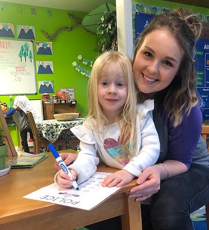 Adult and child coloring a paper with text "POLICE" in a classroom