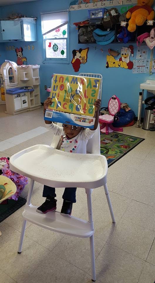 Child in a high chair holding up a colorful alphabet mat