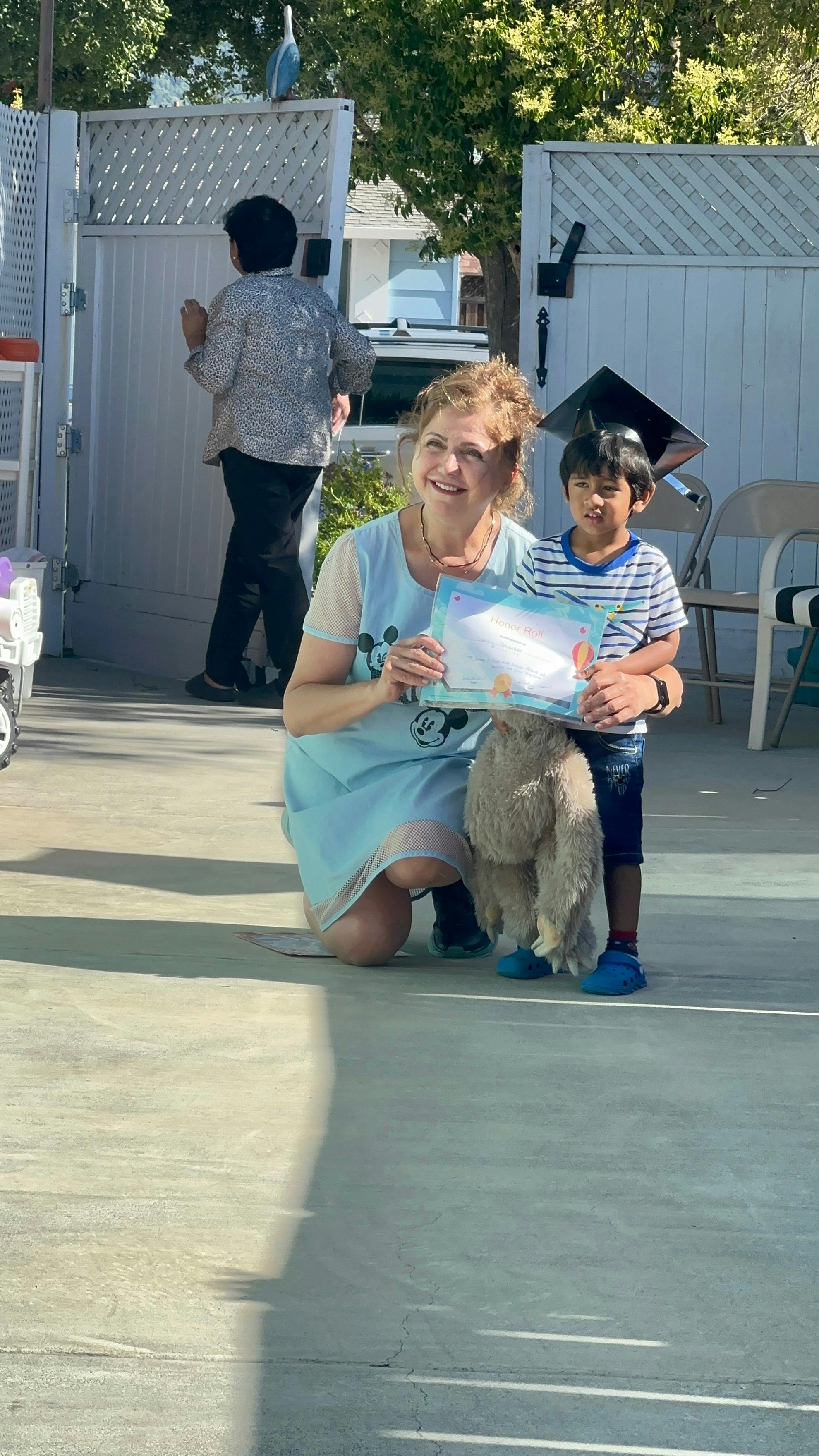 Person kneeling with a child wearing a graduation cap, holding a certificate