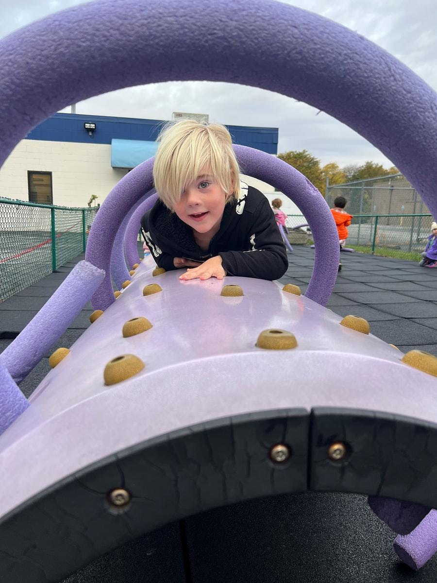 Child looking at camera from inside a purple playground tunnel