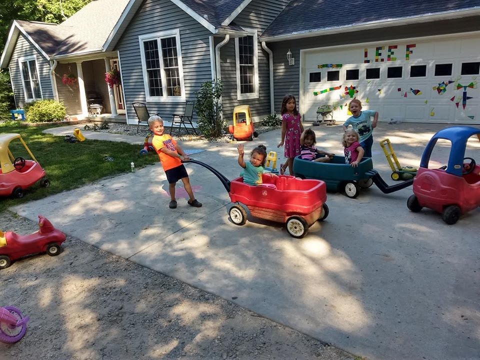 Children playing with wagons and ride-on toys in a driveway