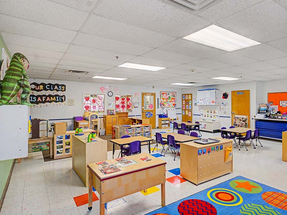 Classroom with small tables and chairs, shelves, and a colorful rug