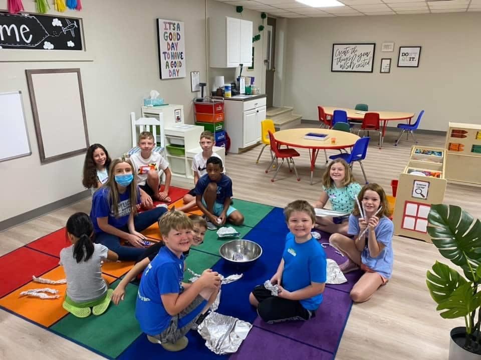 People and children sitting on a colorful rug in a classroom