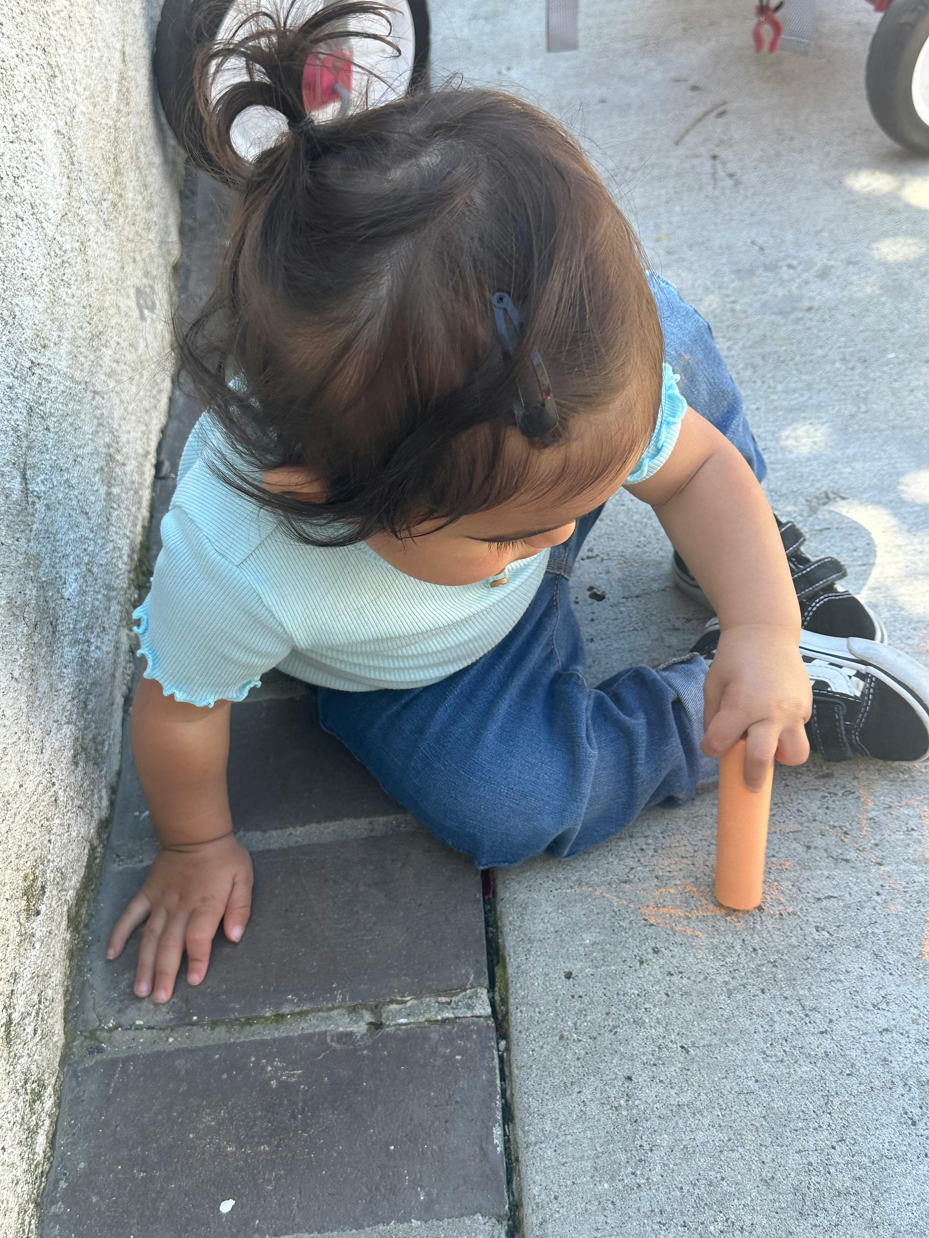 Child sitting on the ground holding a piece of chalk