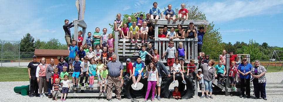 Large group of people and children posing on and around a playground structure