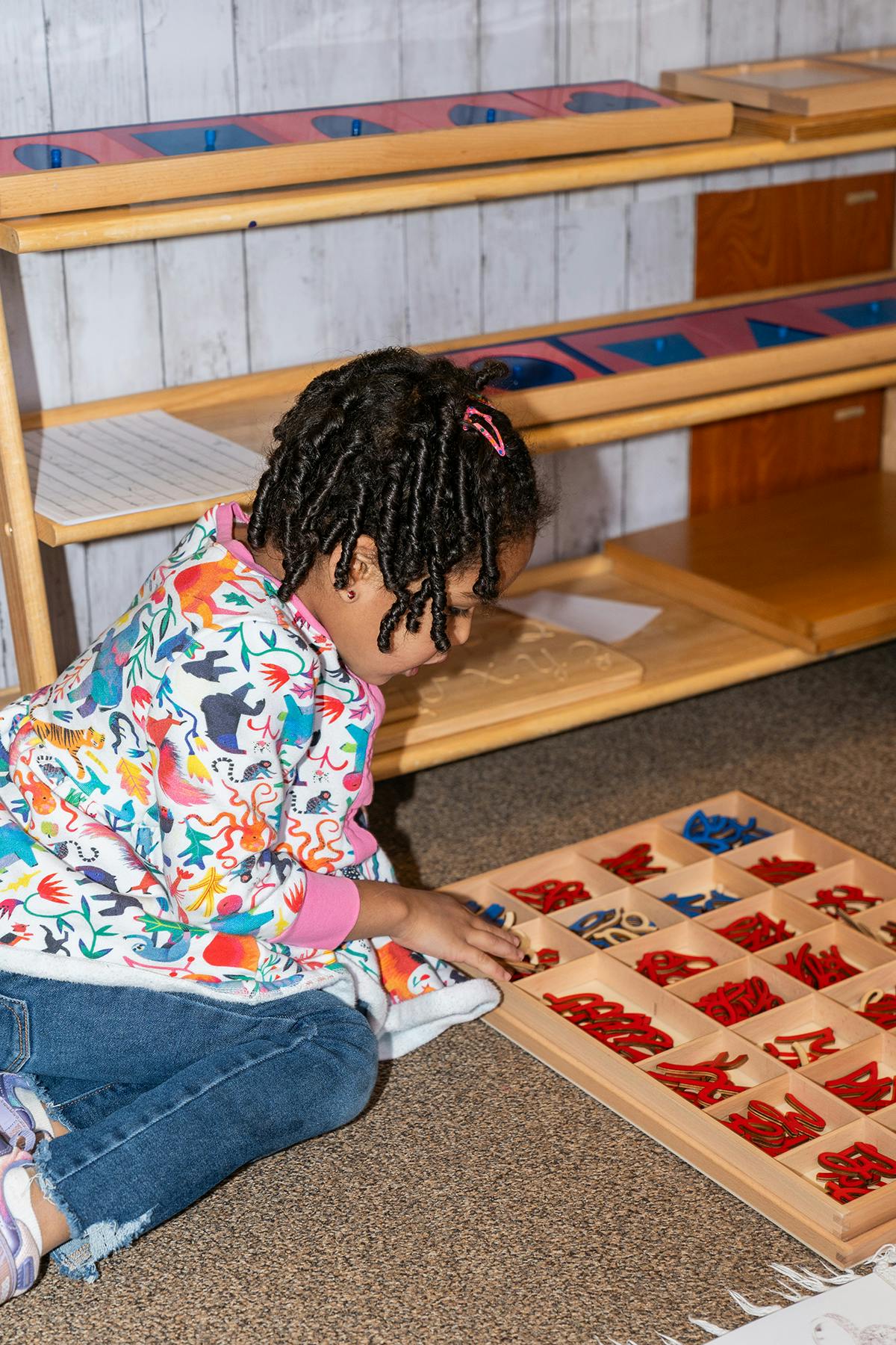 Child playing with a wooden tray of red and blue shapes
