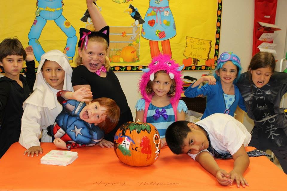 Children in costumes posing around a decorated pumpkin