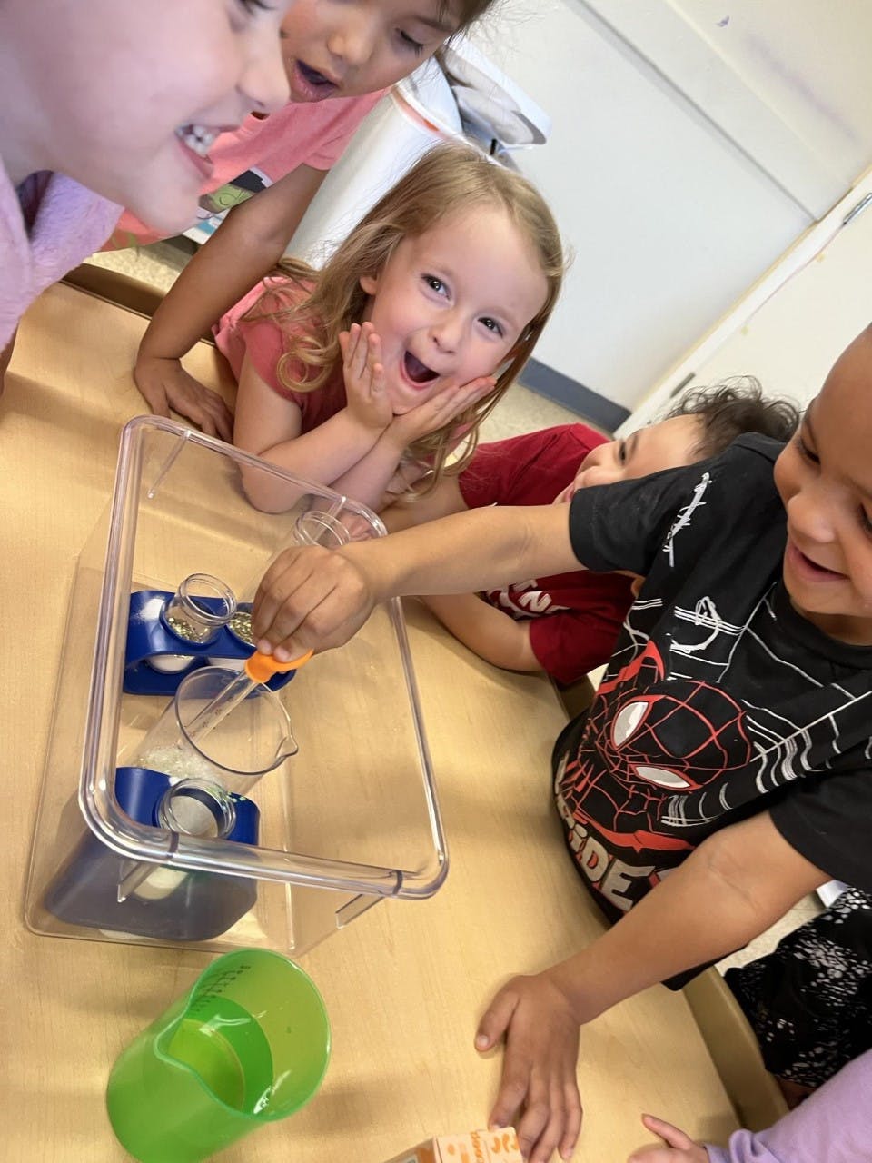 Children gathered around a table, one using a dropper in a clear container