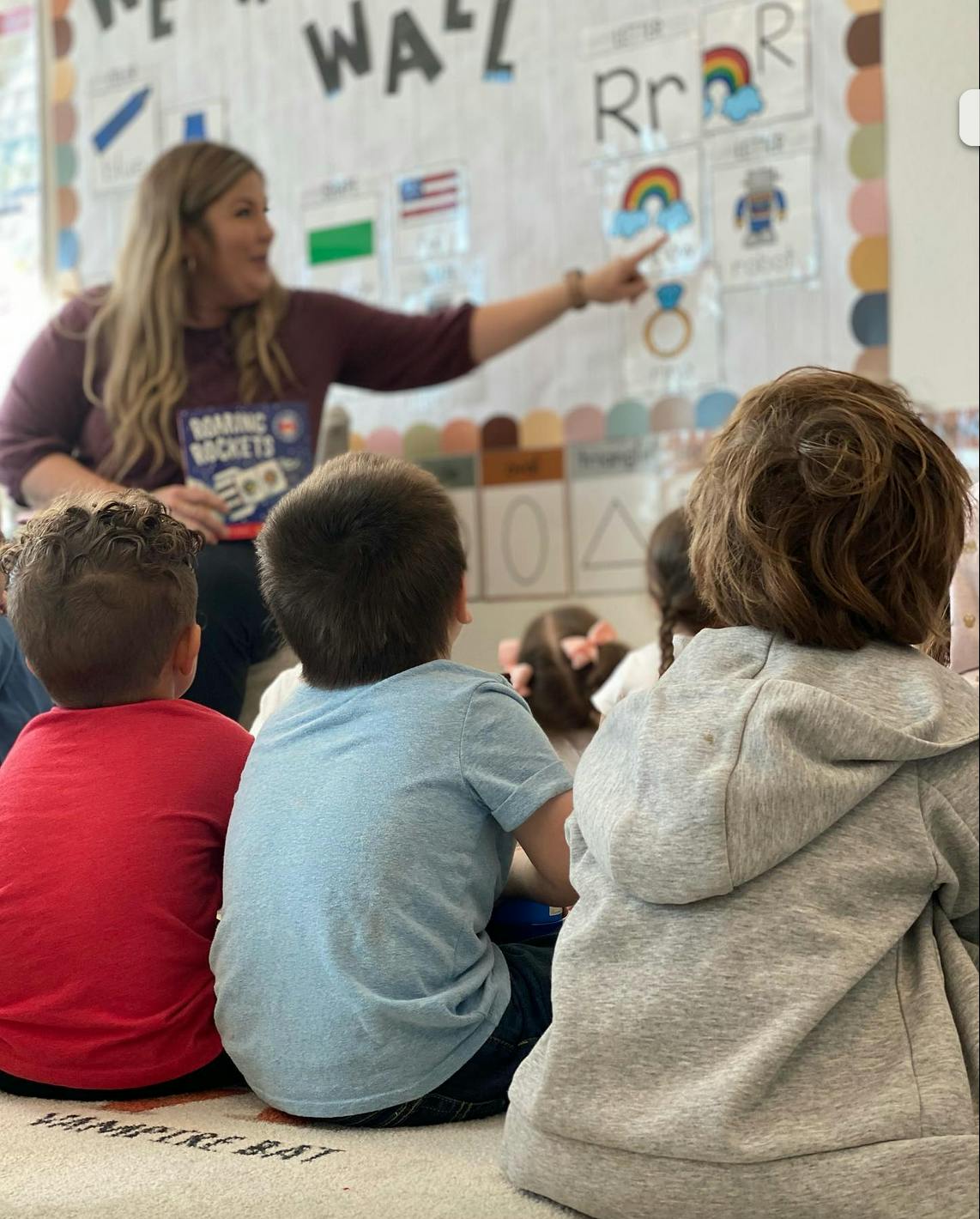 Person pointing at a board in a classroom with children watching