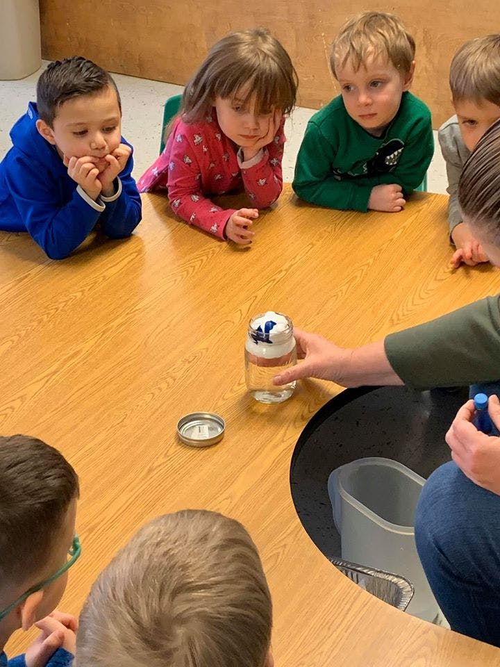 Children gathered around a table looking at a jar