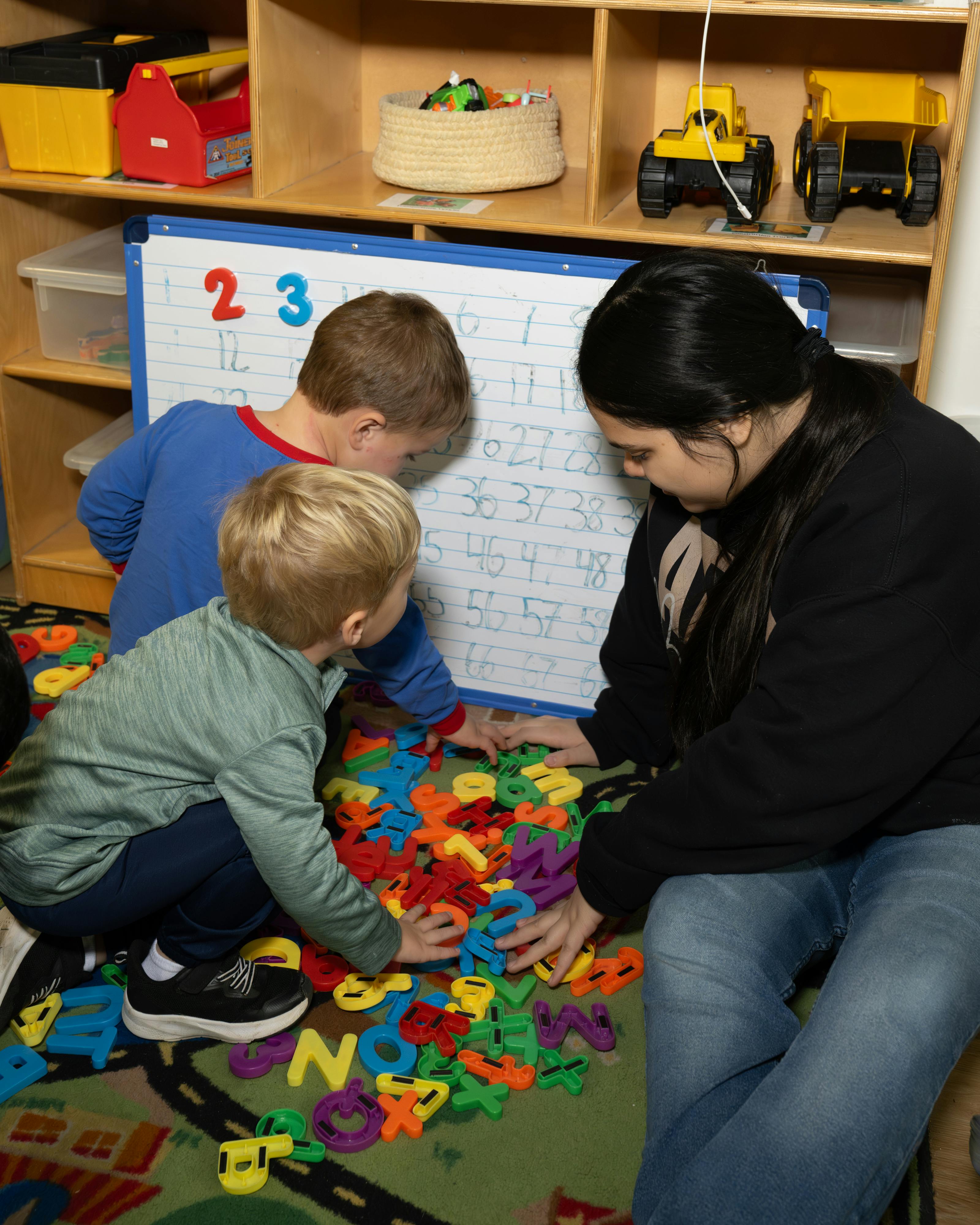 Adult and two children playing with colorful letter toys on a rug