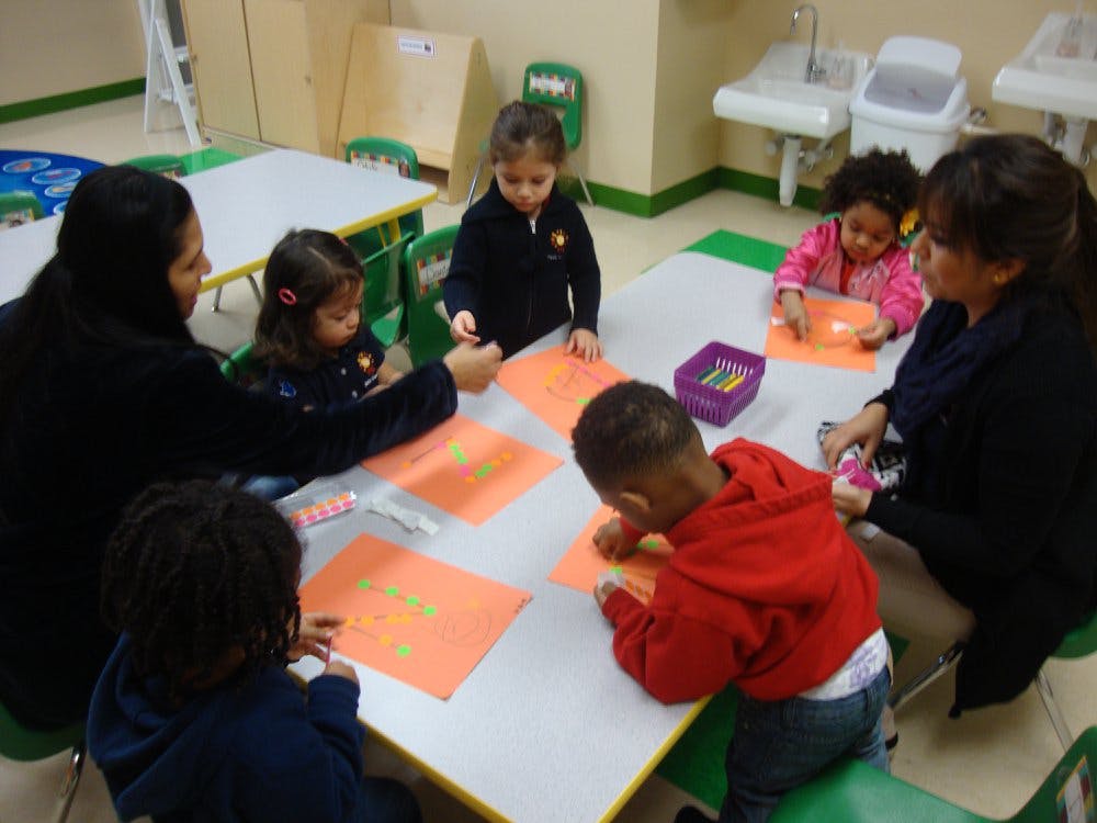 Adults and children sitting at a table doing an activity with orange papers