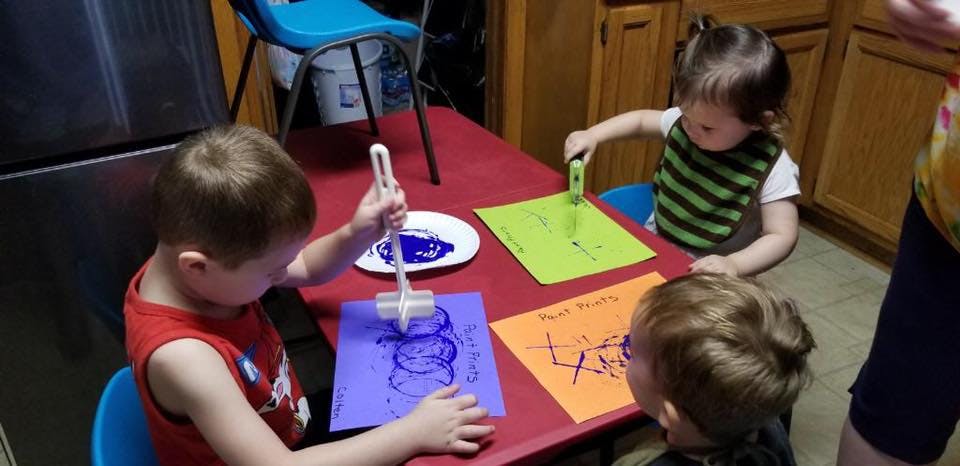 Three children at a table doing crafts with paint and paper