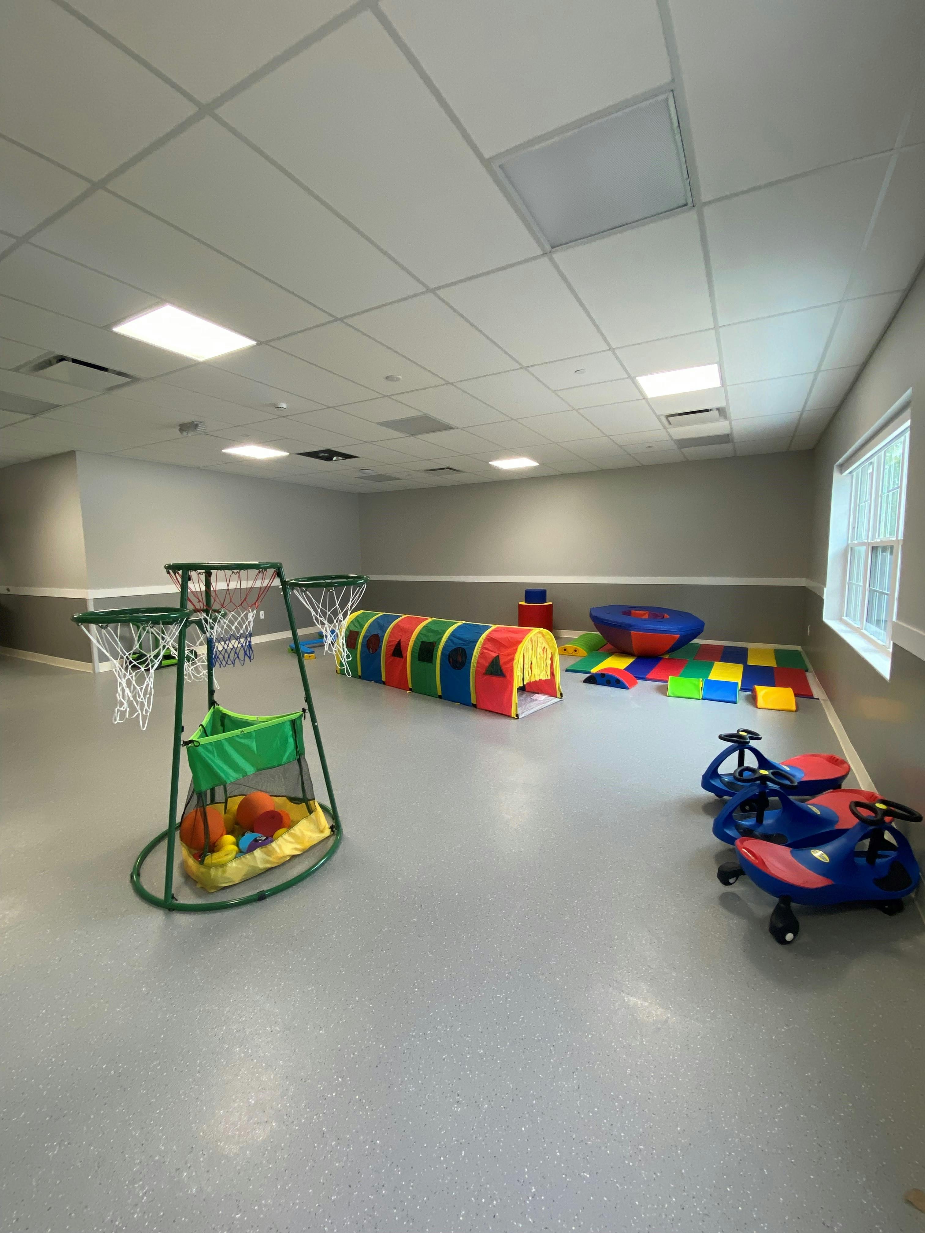Indoor play area with colorful tunnel, basketball hoops, and ride-on toys