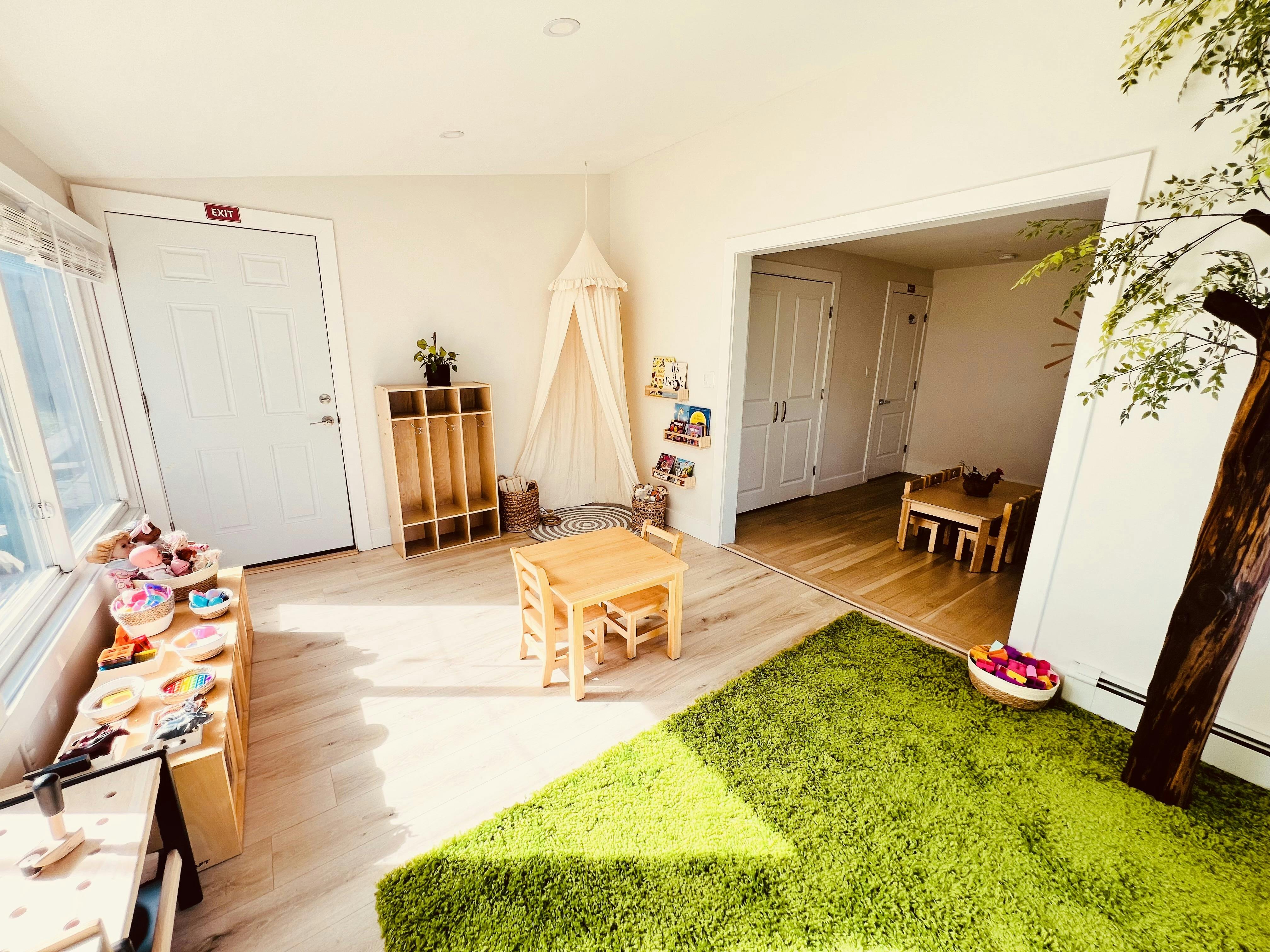Playroom with small wooden tables and chairs, a green rug, and a canopy