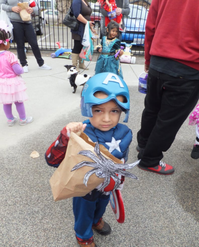 Child in Captain America costume holding a paper bag with a spider decoration