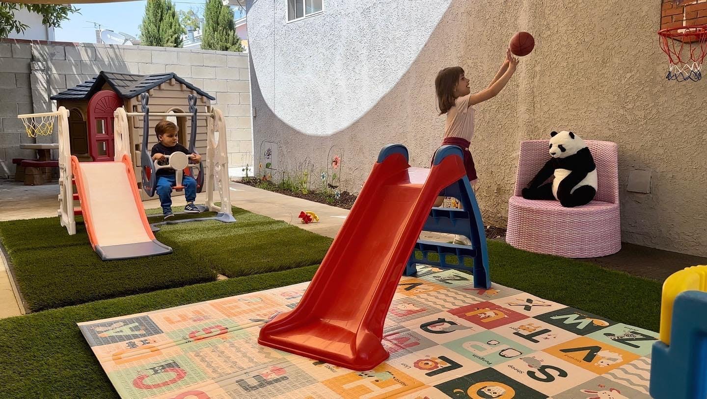 Child on a swing and a person playing basketball in a play area