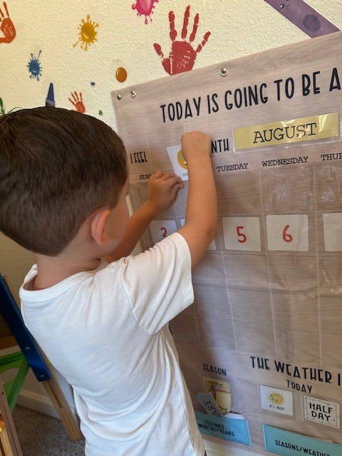 Child placing a card on a fabric calendar with "August" visible