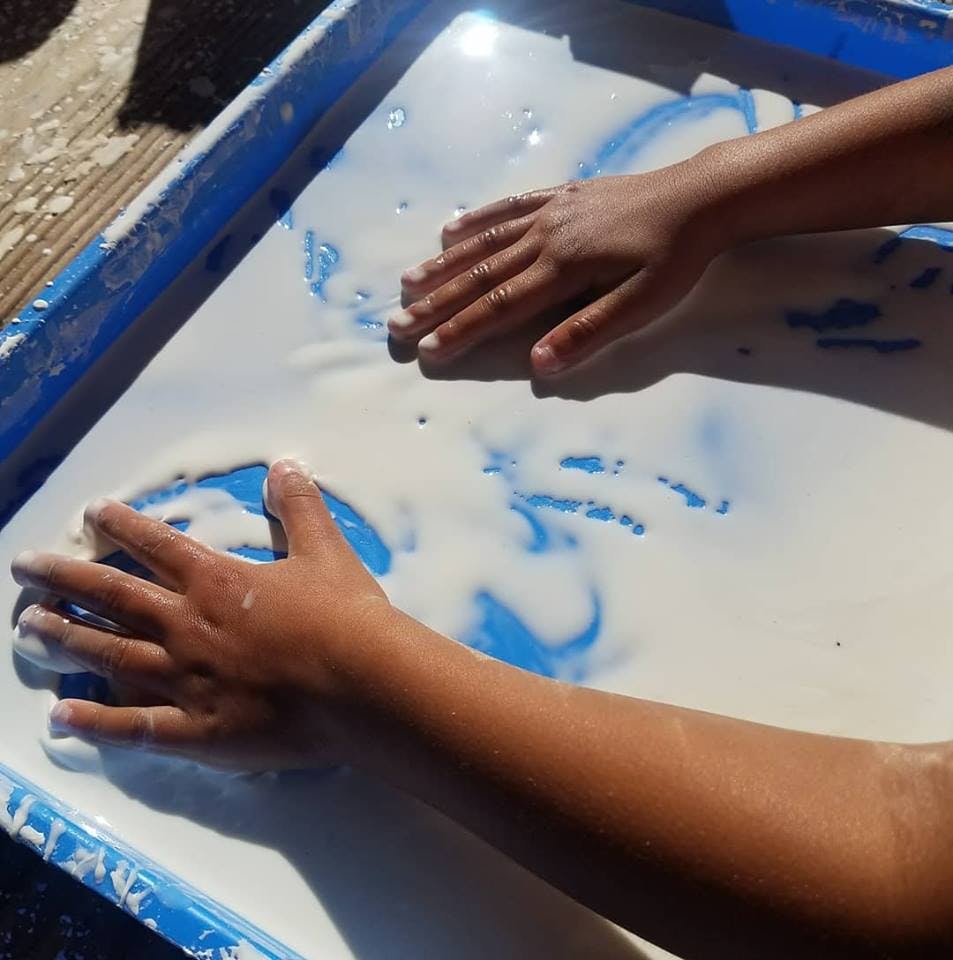 Child's hands playing in a tray with white liquid