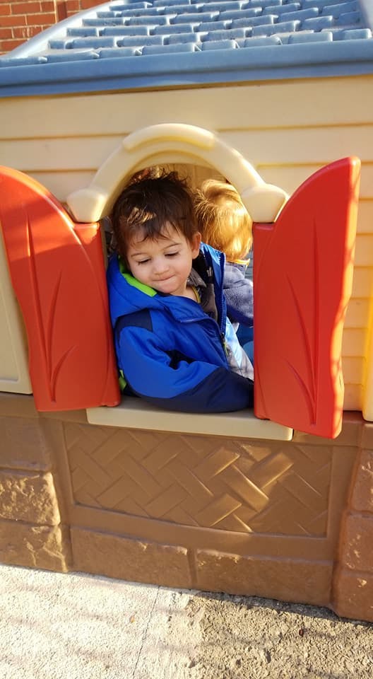 Child in a blue jacket looking out of a playhouse window