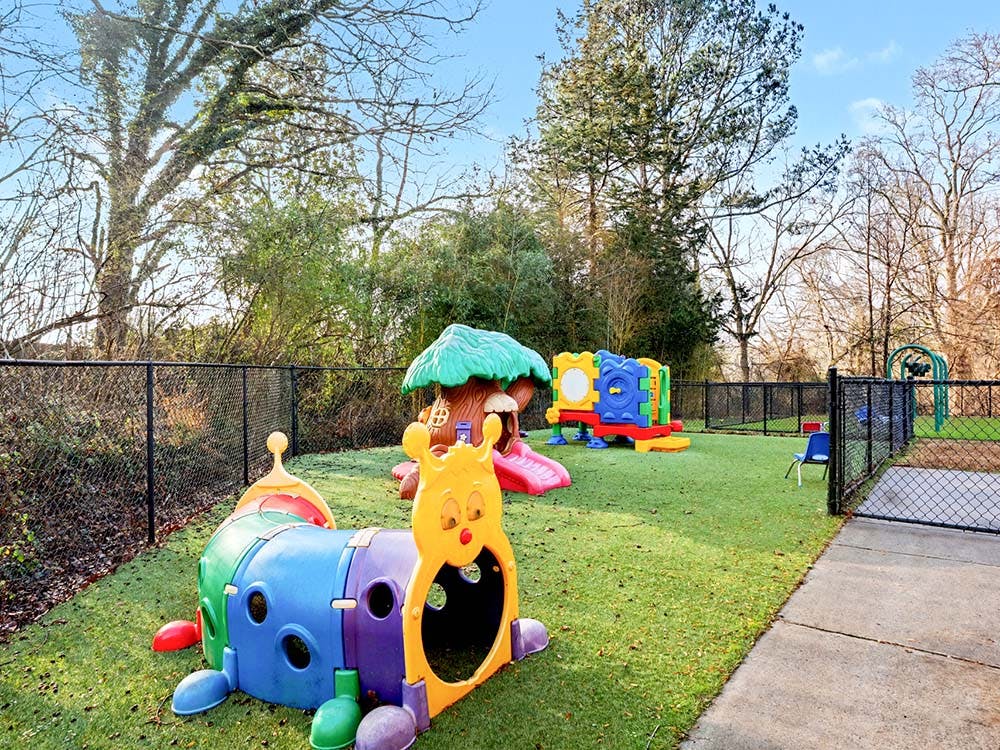 Colorful caterpillar play tunnel and treehouse slide on a playground with a black fence