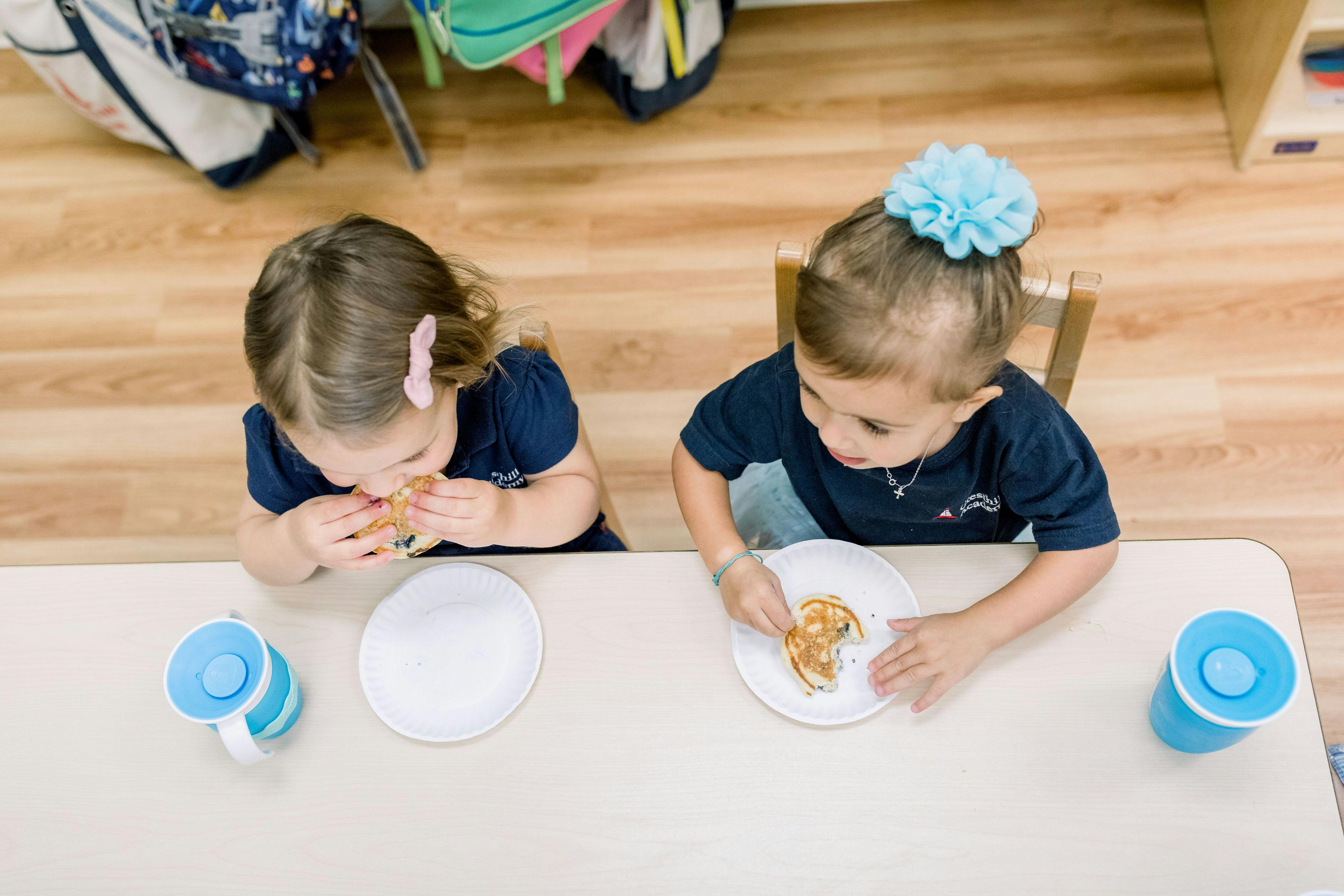 Two children sitting at a table eating pancakes