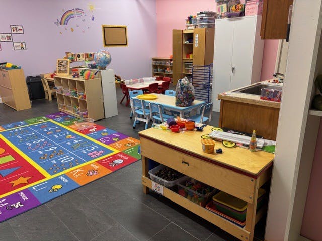 Colorful playroom with a large educational rug, small tables and chairs, and toy storage