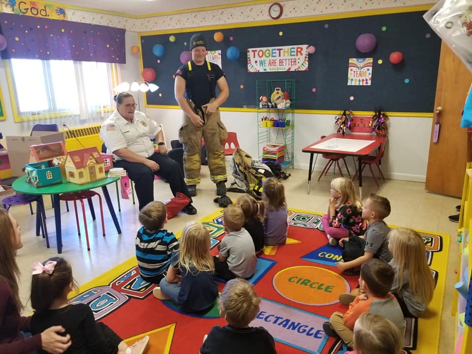 Two adults in uniform with children sitting on a rug in a classroom
