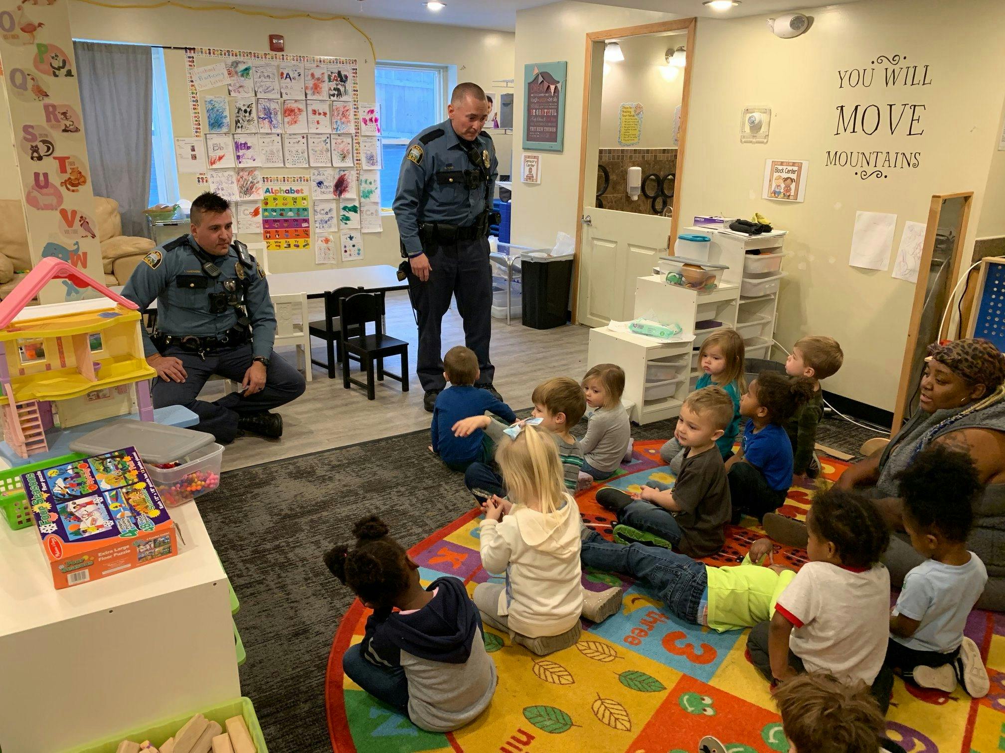Two people in uniform interacting with a group of children in a classroom