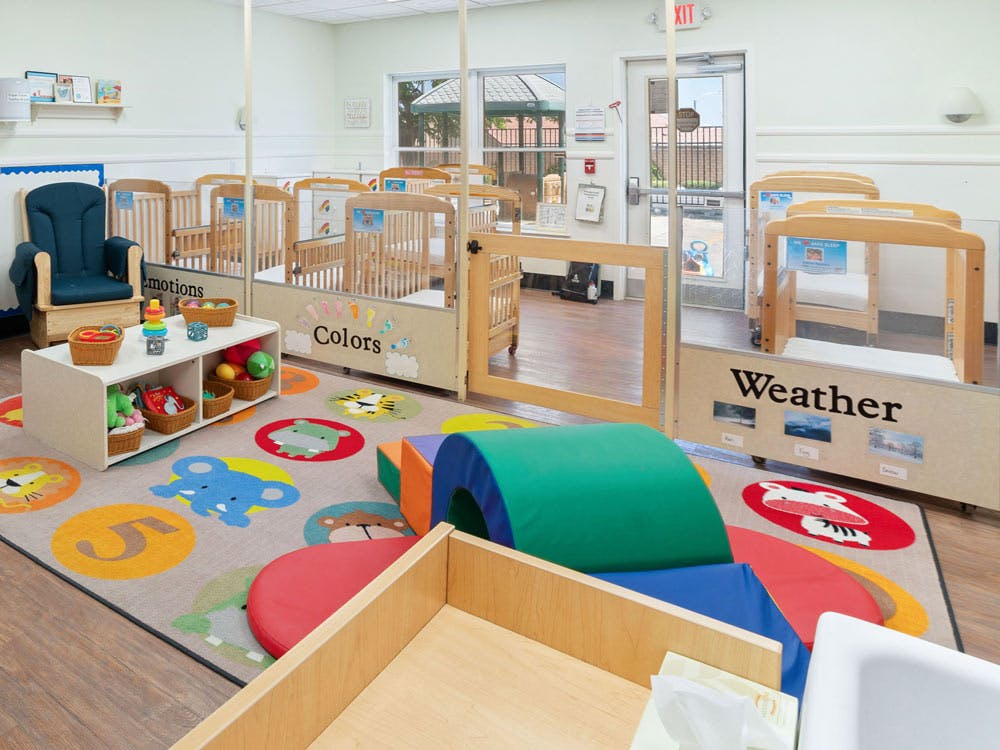 Classroom with cribs, play rug with animal shapes, and play furniture