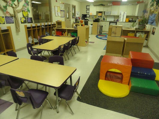 Classroom with tables and chairs, cubbies, and soft play equipment
