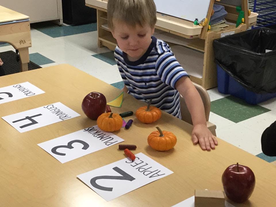 Child at a table with number cards, apples, and pumpkins