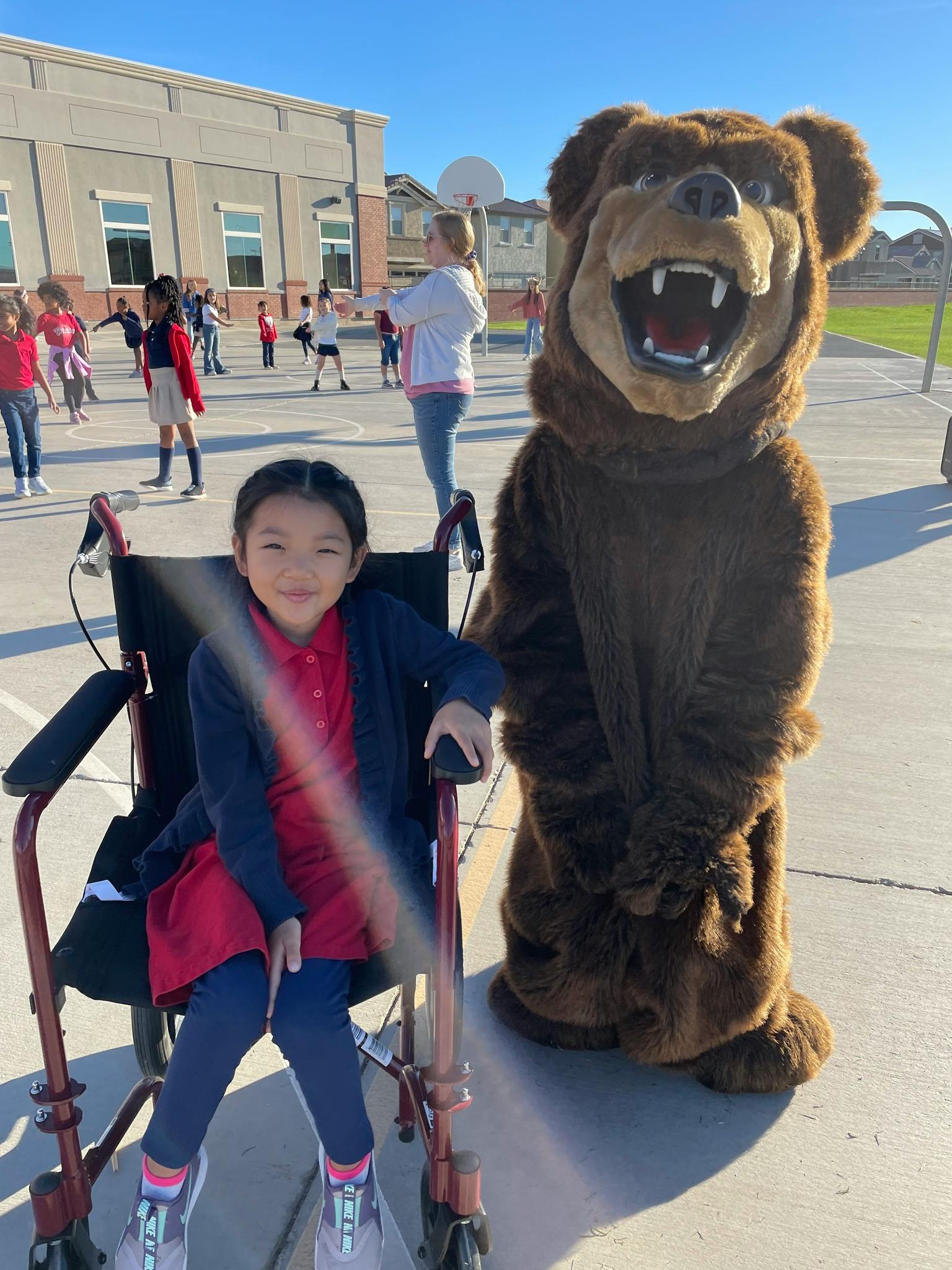 Child in a wheelchair next to a person in a bear mascot costume