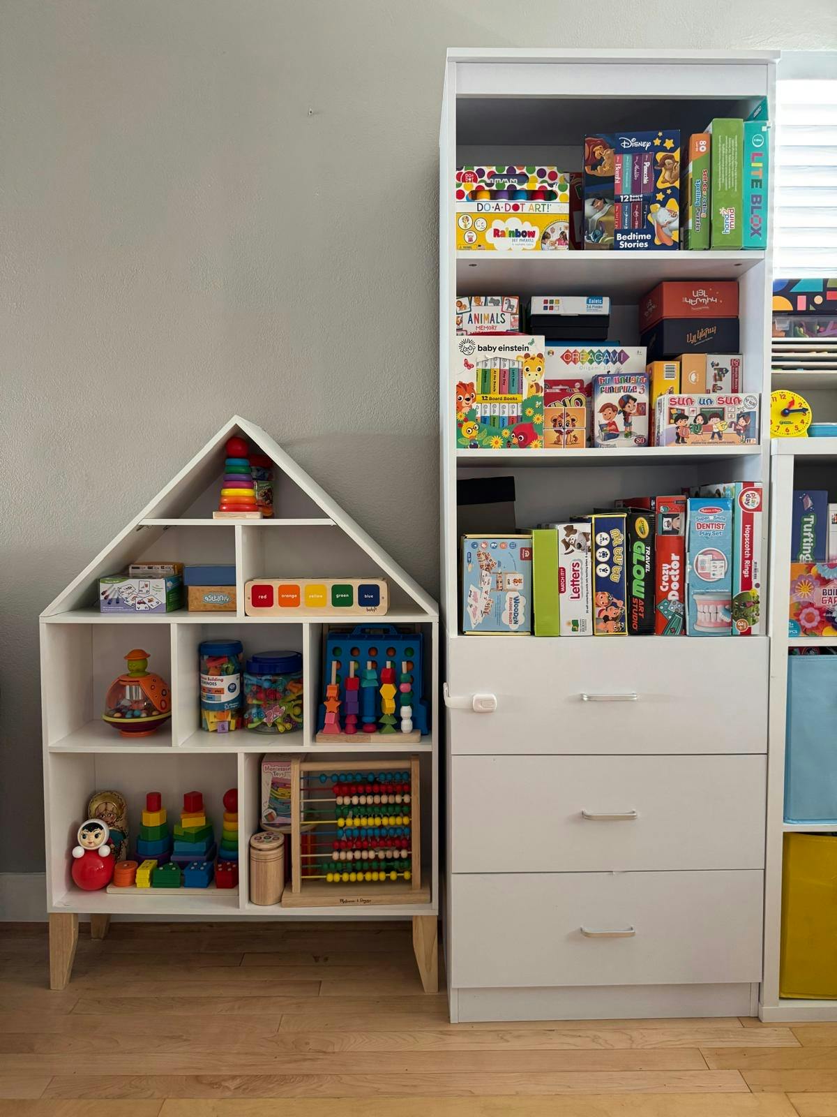 House-shaped bookshelf filled with colorful toys and games next to a white dresser
