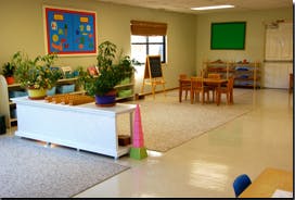 Classroom with plants, small tables and chairs, and a chalkboard