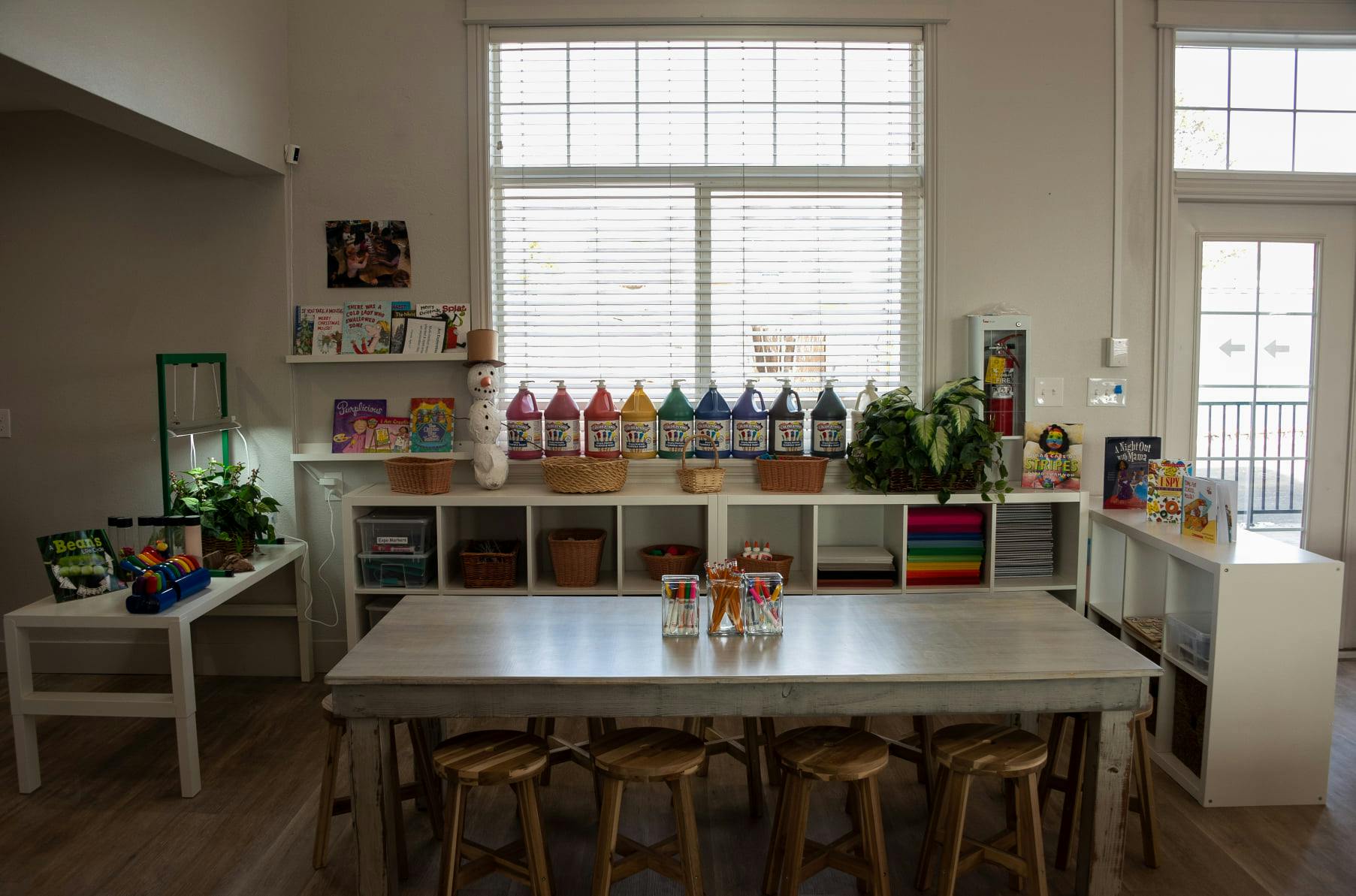 Art studio with a long table and stools, shelves with art supplies
