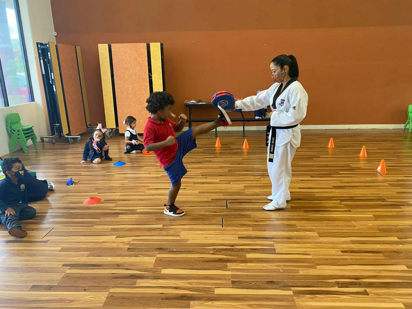 Child kicking a pad held by a person in a martial arts uniform