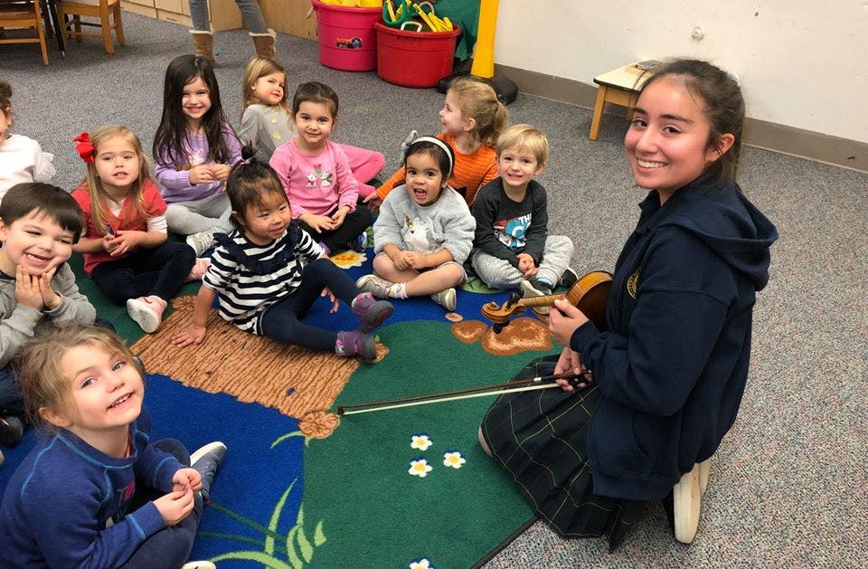 Person playing violin for a group of children in a classroom